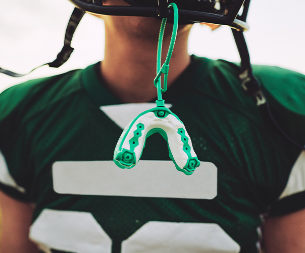 Teen with a green athletic mouthguard hanging from football helmet